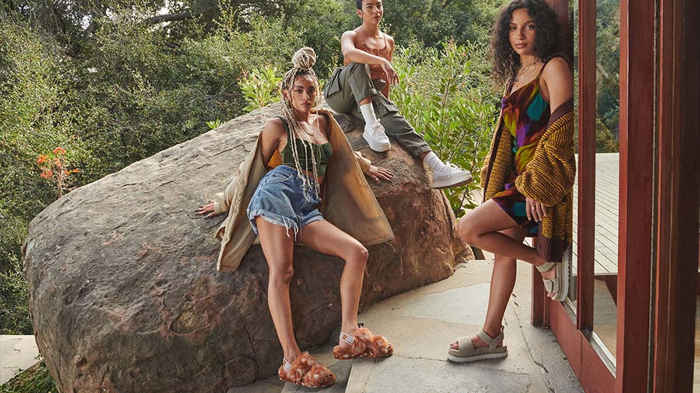 Three women in UGG shoes posing near a rock.