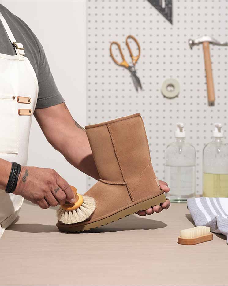 Worker refreshing an UGG Classic boot with tools on a table.