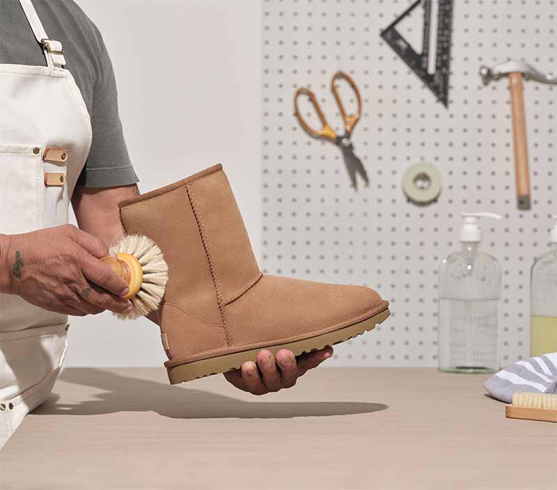 Worker refreshing an UGG Classic boot with tools on a table.
