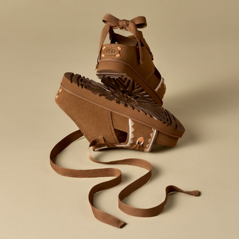 A pair of UGG women's sandals, sitting against a beige backdrop.