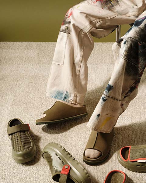 Person sitting in a chair wearing UGG Otzo Slide with other shoes scattered on the floor.