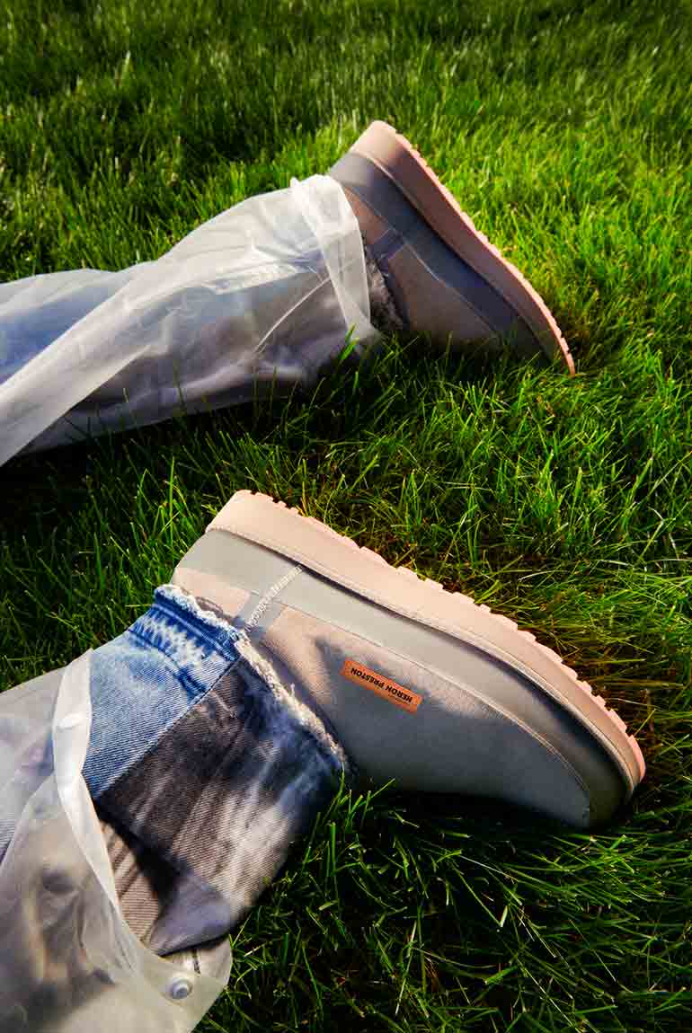 Close-up of a person's feet in the UGG X HP Clsasic Short Zip Waterproof while lying in the grass.