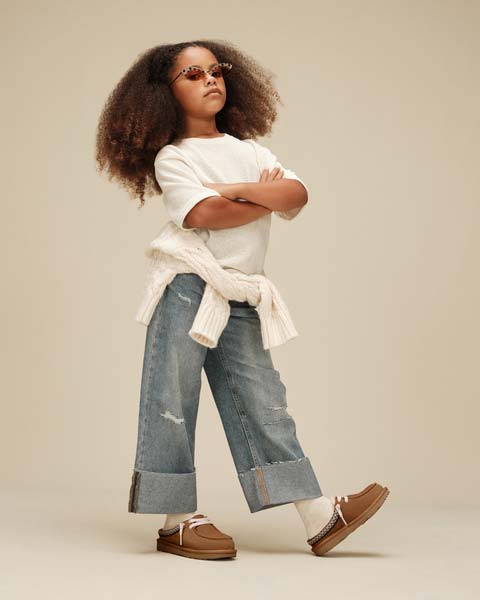 Kid standing against a tan background, wearing the Tasman Mule in chestnut color.