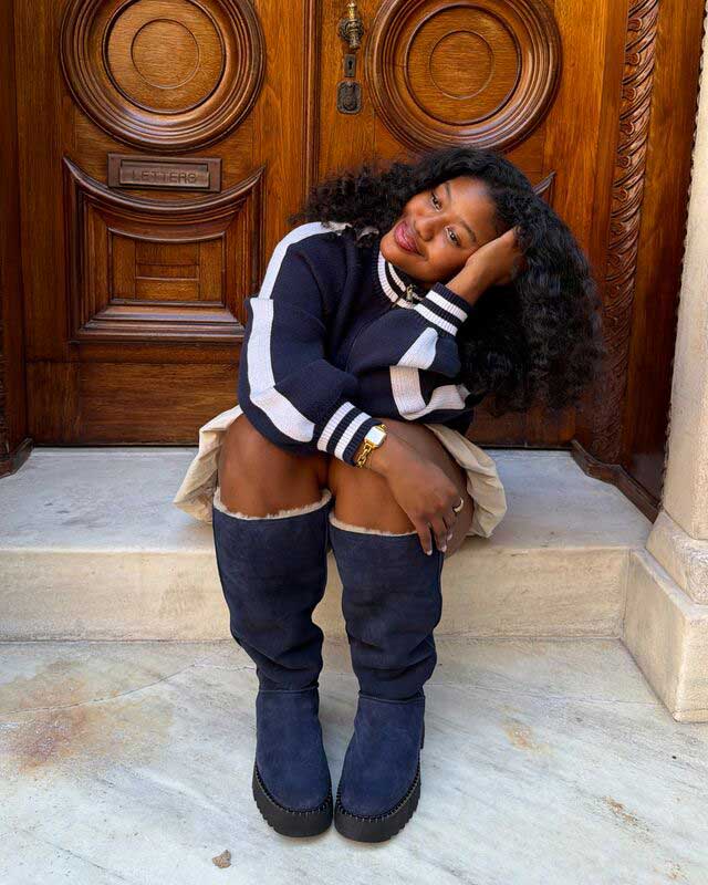 A feminine person seated on the front step of a porch wearing the new Uptowner Tall Boot and a matching fit.
