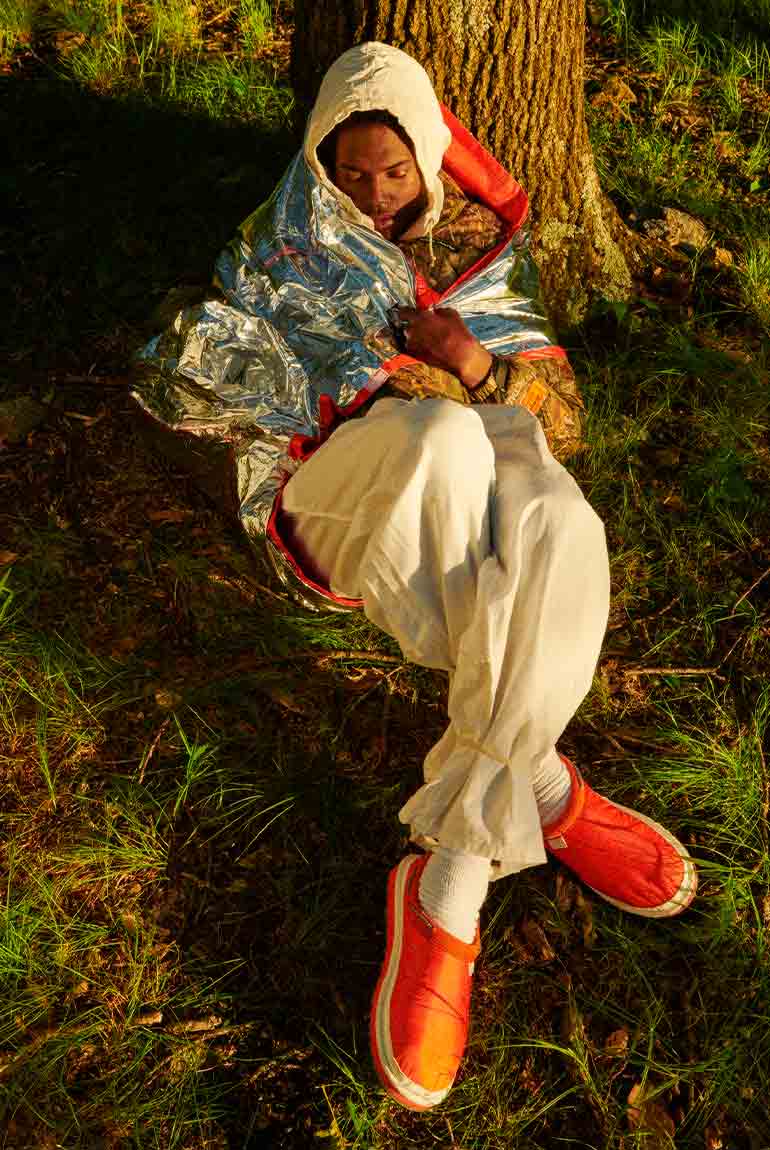Boy curled up against tree wearing the UGG X HP Tasman in orange.