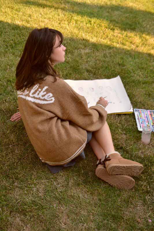 Une personne féminine se prélassant sur une pelouse, portant un chandail UGG confortable et des bottes UGG.