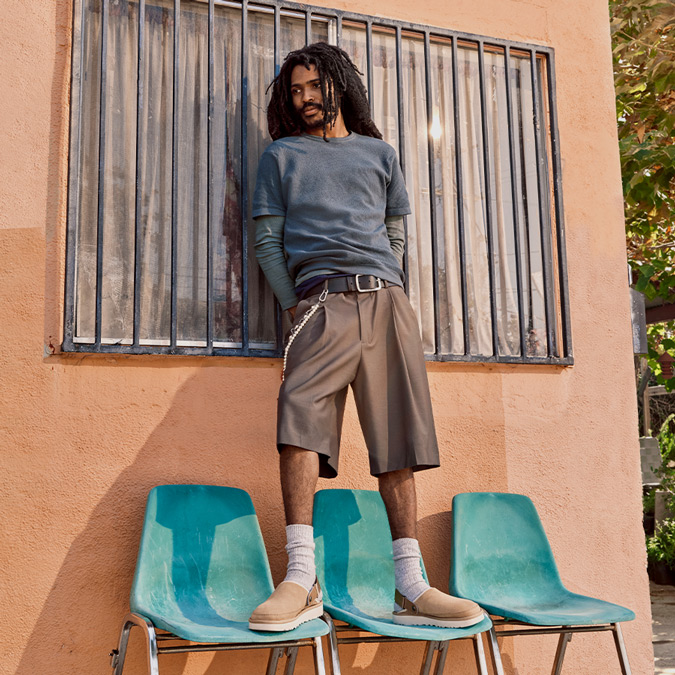 A lifestyle image of a model with dreadlocks stood on a chair wearing the Goldencoast Clogs.