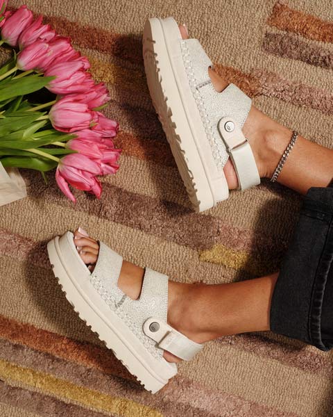 Une photo de sandales UGG portées par des pieds manucurés à côté d’un boquet de tulipes fraîches et éclatantes.