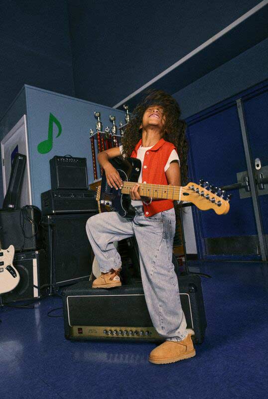 Un enfant jouant de la guitare dans la salle de musique d’une école tout en portant des chaussures UGG.