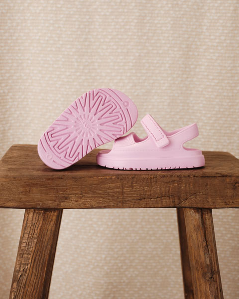 Une paire de sandales GoldenGlow pour enfants posée sur un tabouret en bois avec un fond neutre.