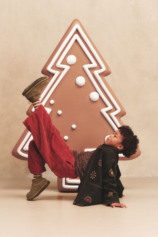 A boy posing wearing our UGG Classic Ultra Stretch Cuff close to a decorative Christmas tree.