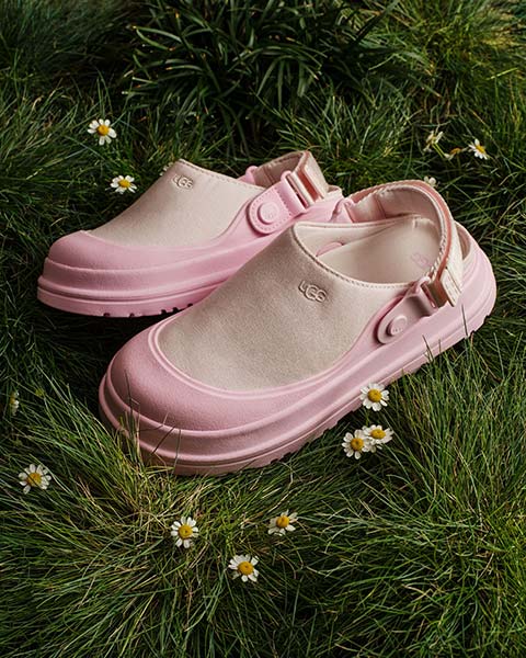A pair of UGG shoes on display in the grass with small flowers.