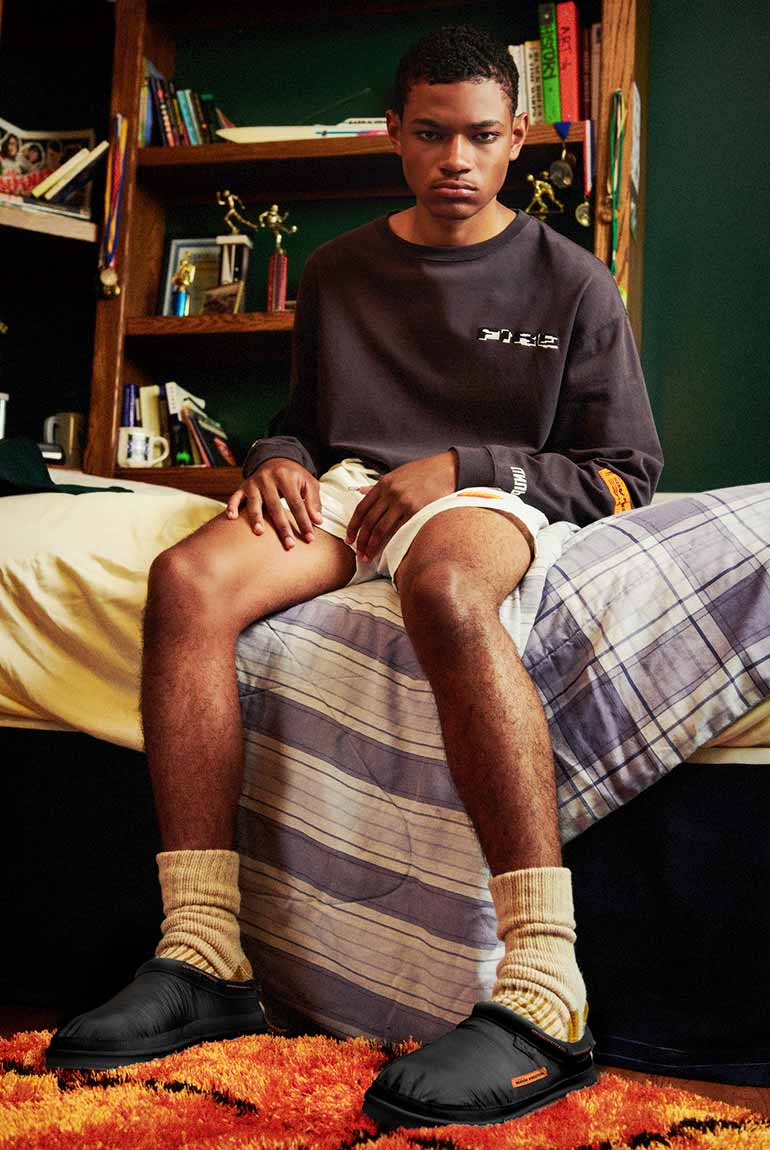 Boy sitting on bed wearing the UGG X HP Tasman in black.