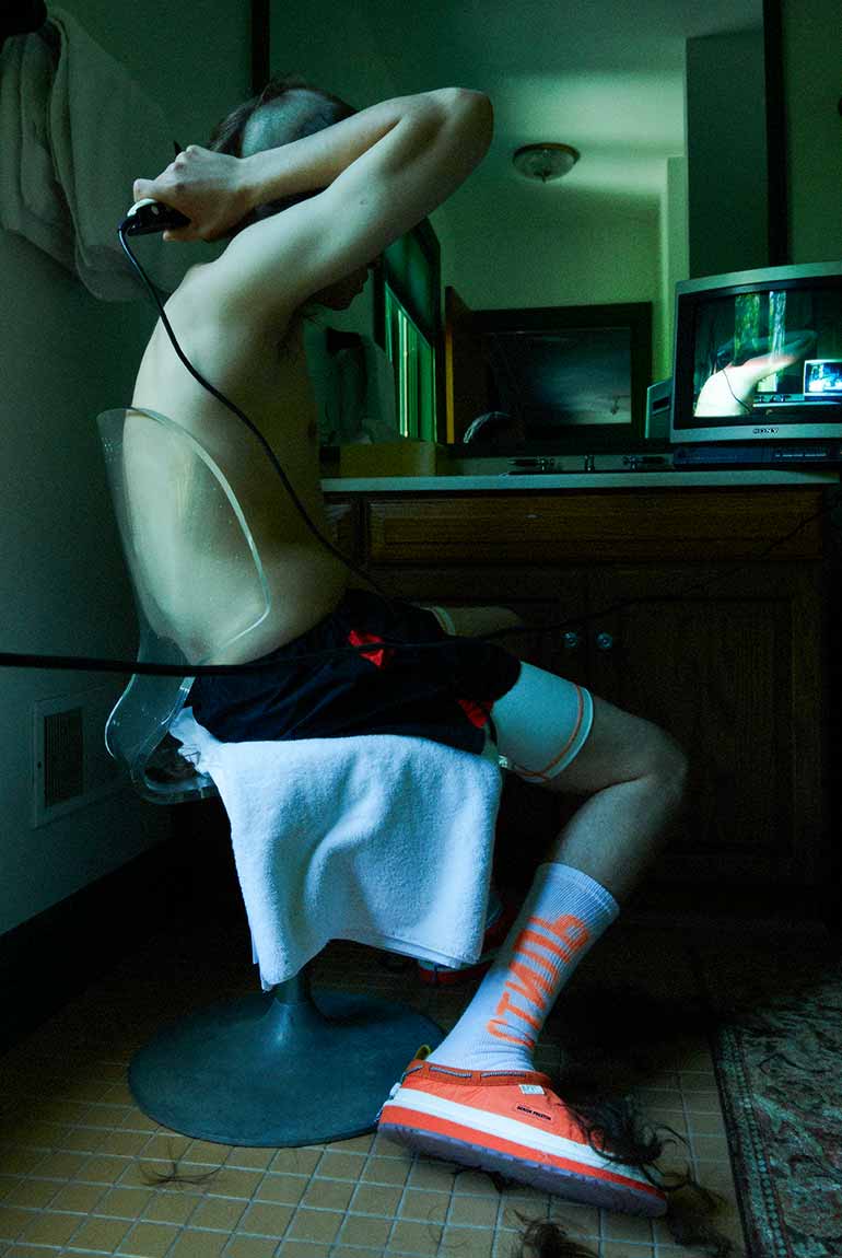 Boy shaving his head while wearing the UGG X HP Tasman in orange.