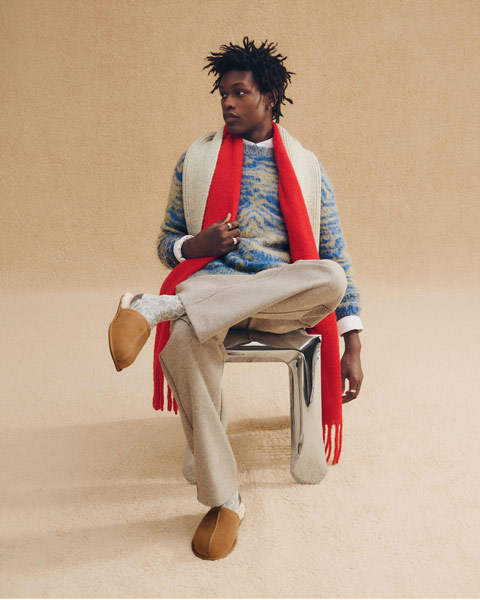 A masculine person wearing UGG slippers and a matching, cozy fit while lounging in a metallic chair.
